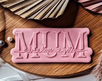 Puede incluir: Sellos de arcilla polimérica rosa con la palabra "MUM" y el texto "I love you" en una fuente cursiva.