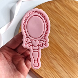 Puede incluir: Cortador de galletas de plástico rosa en forma de espejo de mano con un corazón en la parte superior del mango.