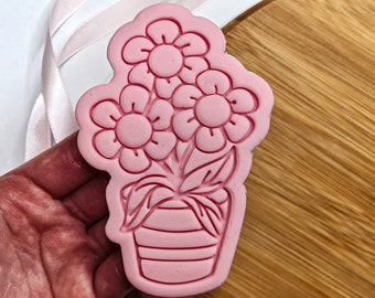 Puede incluir: Cortador de galletas de plástico rosa en forma de planta en maceta con tres flores. Las flores tienen un diseño simple de margarita.
