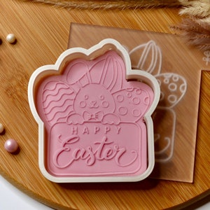 May include: Pink plastic cookie cutter shaped like a bunny holding a sign that says "Happy Easter".