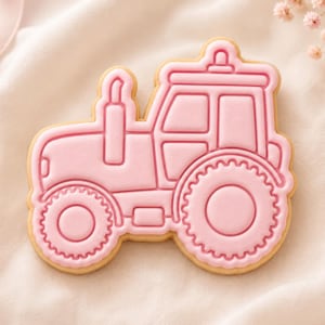 May include: A tractor-shaped sugar biscuit decorated with smooth, light pink icing. The icing features embossed outlines of the tractor body, a tall exhaust pipe, a cabin with windows, and large, textured wheels with a distinct tread pattern.