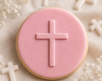 May include: A round cookie with a pink frosting layer, featuring a cross imprint. Several small white cross-shaped decorations are scattered around the cookie. The cookie has a light brown edge.