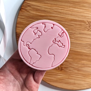 May include: A pink silicone mould shaped like the Earth. The mould has a detailed outline of the continents and oceans.