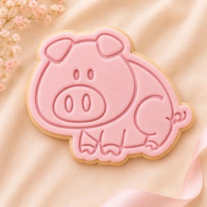 May include: A pig-shaped sugar cookie decorated with smooth light pink icing. The icing features embossed outlines of a pig's face, ears, snout, body, and a curled tail. The cookie has a visible tan-colored baked edge around the pink icing layer.