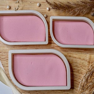 May include: Three white plastic leaf-shaped molds with pink resin inside. The molds are on a wooden surface.