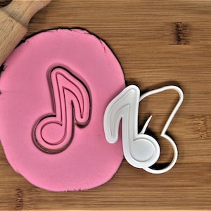 May include: White plastic cookie cutter in the shape of a musical note. The cutter is on a wooden surface with pink play dough underneath.
