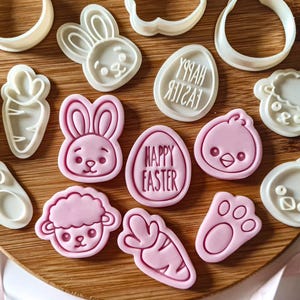 May include: A set of 12 pink and white plastic cookie cutters shaped like Easter-themed animals, carrots, and eggs. The cutters include a bunny, a chick, a lamb, a carrot, a paw print, and an egg with the text "Happy Easter".