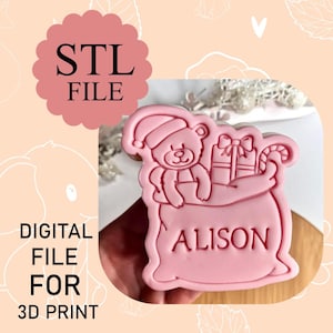 May include: Pink STL file for 3D print of a teddy bear in a Santa hat holding gifts and a candy cane in a sack. The name "ALISON" is printed on the sack. The words "STL FILE" and "DIGITAL FILE FOR 3D PRINT" are also visible.