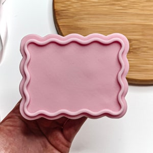 Puede incluir: Molde de silicona rosa con un borde ondulado. El molde tiene forma rectangular y una superficie lisa.