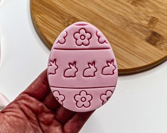 Puede incluir: Molde de silicona rosa en forma de huevo de Pascua con un diseño de conejos y flores.