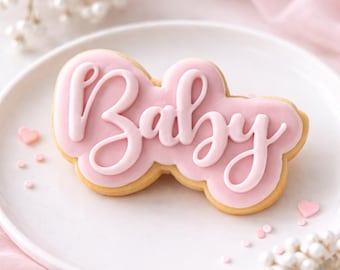 Può includere: Un biscotto glassato rosa a forma di nuvola con la parola "Baby" scritta in corsivo. Il biscotto è su un piatto bianco, con piccole decorazioni a forma di cuore rosa e fiori decorativi sullo sfondo.