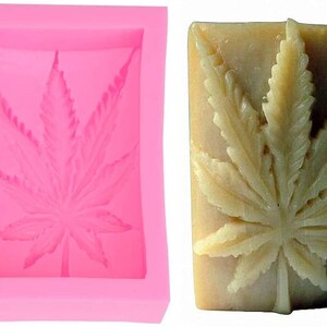 May include: A pink silicone mold with a rectangular shape, featuring a detailed cannabis leaf design. Next to it is a bar of soap with the same leaf design carved into it, showcasing the finished product.