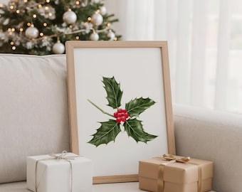 Puede incluir: Una impresión enmarcada con una ilustración de acuarela de acebo con hojas verdes y bayas rojas. Dos regalos envueltos, uno blanco y otro marrón, se colocan frente al marco. Un árbol de Navidad con luces se encuentra en el fondo.