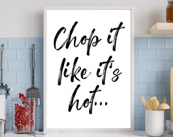 May include: A white framed print with black text that reads "Chop it like it's hot..." The print is hanging on a white tiled wall in a kitchen.