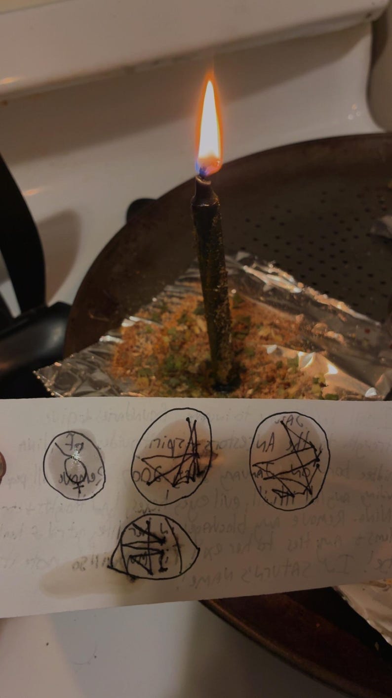Peut inclure: Une bougie noire avec une flamme allum&eacute;e se trouve dans une po&ecirc;le en m&eacute;tal sur du papier aluminium recouvert d'herbes. Au premier plan, une bande de papier blanc pr&eacute;sente quatre symboles circulaires dessin&eacute;s &agrave; la main avec des lignes noires.
