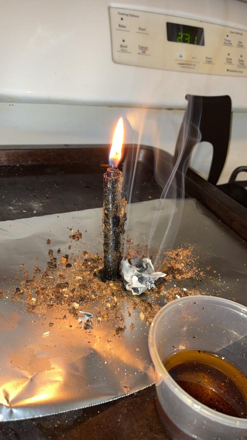 Peut inclure: Une bougie noire allum&eacute;e est pos&eacute;e sur une feuille d'aluminium, entour&eacute;e de d&eacute;bris v&eacute;g&eacute;taux bruns et d'un petit morceau de papier blanc froiss&eacute; d&eacute;gageant de fines volutes de fum&eacute;e, avec un gobelet en plastique transparent contenant un liquide ambr&eacute;.
