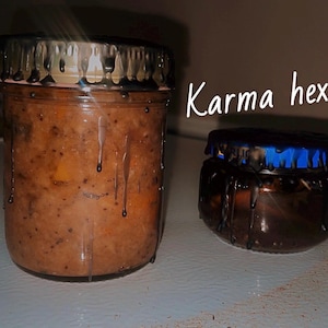 Peut inclure: Deux bocaux en verre avec des coulures marron foncé autour des couvercles. Le plus grand bocal contient un mélange brun. Le plus petit bocal a un couvercle bleu. Le texte "Karma hex" est écrit en blanc.