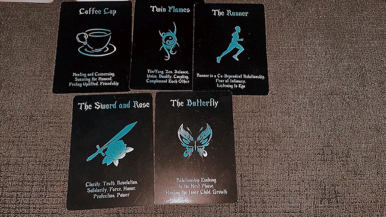 May include: Five rectangular oracle cards with black backgrounds and cyan blue illustrations and text. The cards feature titles and descriptions including Coffee Cup, Twin Flames, The Runner, The Sword and Rose, and The Butterfly, each with a corresponding icon.