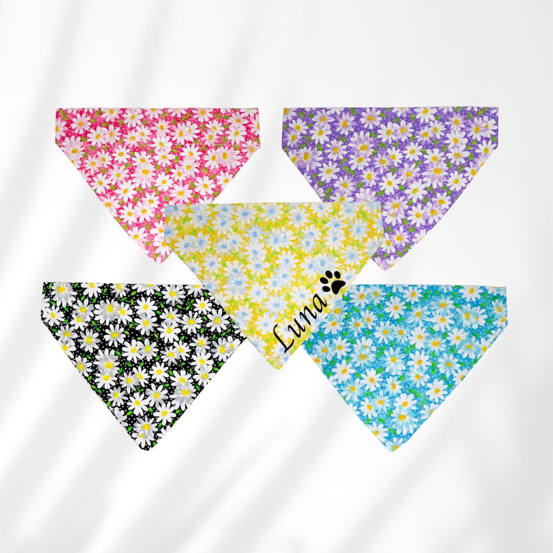 May include: Five dog bandanas with a daisy print. The bandanas are in pink, purple, yellow, black, and blue. One bandana has the name "Luna" and a paw print.