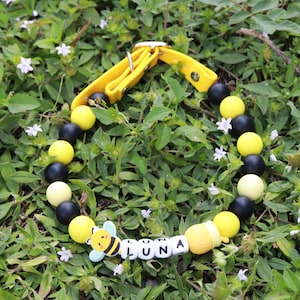 May include: A yellow and black silicone beaded dog collar with a bee charm and the name "LUNA" spelled out in white beads.