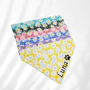 May include: A stack of colorful dog bandanas with a daisy print. The bottom bandana is yellow with a black paw print and the name "Luna" printed on it.