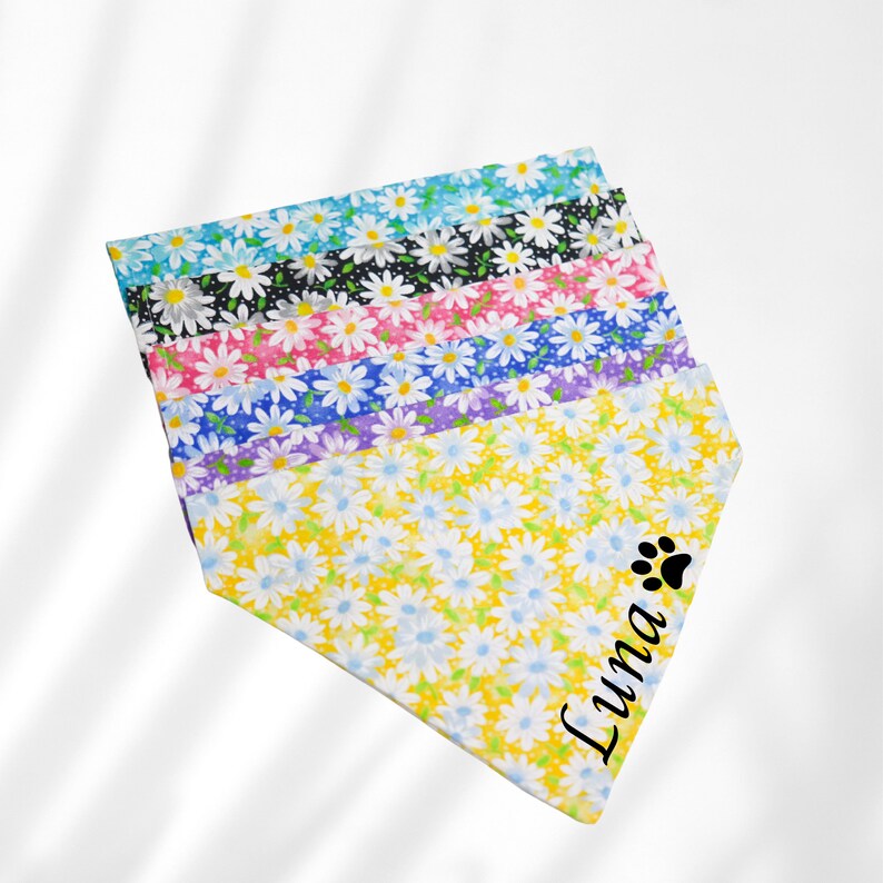 May include: A stack of colorful dog bandanas with a daisy print. The bottom bandana is yellow with a black paw print and the name "Luna" printed on it.
