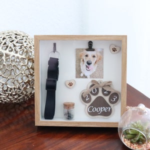 Könnte beinhalten: Eine hölzerne Schattenbox zum Gedenken an einen Hund namens Cooper. Die Box enthält ein Foto des Hundes, ein Halsband, einen Pfotenabdruck mit dem Jahr 2023 und ein kleines Aschegefäß.