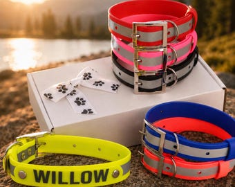 May include: A collection of waterproof dog collars in red, pink, black, blue, orange, and neon yellow, featuring silver metal buckles and reflective strips. One yellow collar displays the name WILLOW in black letters. A white bow with paw prints is included.