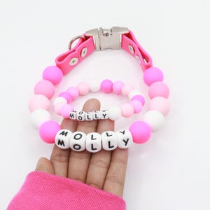 May include: Pink silicone dog collar with a silver buckle and pink and white beads spelling out the name "MOLLY".