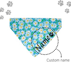May include: Blue dog bandana with a white daisy print. The bandana has a black dotted circle with the word "Name" and a paw print inside. The text "Custom name" is below the circle.