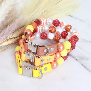 May include: Three colorful beaded dog collars in yellow, orange, and red. The collars are made of different materials, including leather and beads.