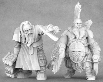 Puede incluir: Dos figuras de enanos detalladas impresas en 3D. Una figura empuña un martillo, la otra un escudo y una espada. Ambos tienen largas barbas y están en posición de combate. Las figuras son en tonos grises.