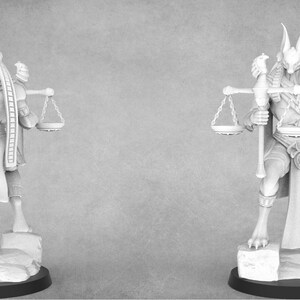 May include: A white painted miniature figurine of an Egyptian god with a jackal head, holding scales and a staff. The figure is standing on a rocky base.