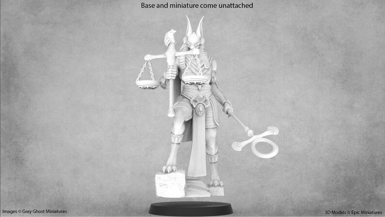 May include: A white, detailed miniature of a jackal-headed figure holding a scale and a staff. The figure is wearing a skirt and a necklace. The miniature is standing on a square base.