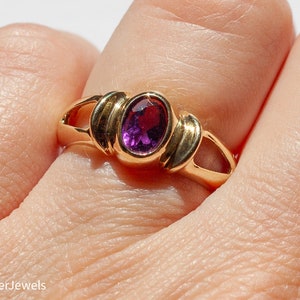 May include: A gold ring with a purple oval gemstone set in a simple, elegant design.