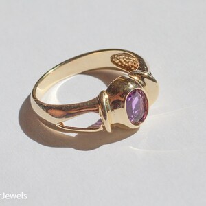May include: A gold ring with a purple gemstone set in a bezel setting. The ring has a unique design with a twisted band.