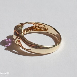 May include: A gold ring with a purple gemstone set in a knot design. The ring is marked "14K" on the inside of the band.