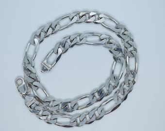 May include: A silver-colored Figaro chain necklace. The necklace features a pattern of three small circular links followed by one elongated oval link. The clasp is visible at the end of the chain.