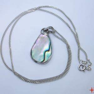 May include: Silver necklace with a pear-shaped pendant. The pendant features a shimmering, iridescent abalone shell with shades of blue, green, and purple. The chain is a delicate curb link style, and the clasp is visible.