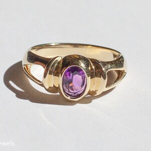 May include: A gold ring with a purple oval gemstone set in a twisted band.