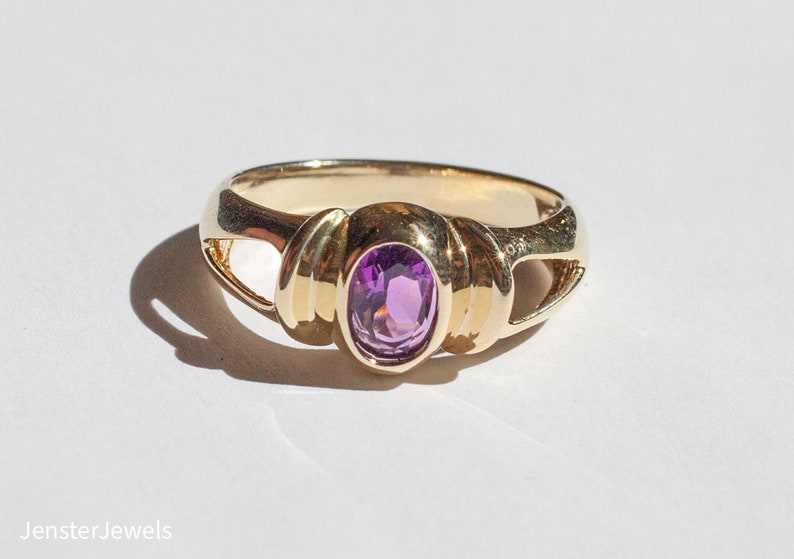 May include: A gold ring with a purple oval gemstone set in a twisted band.