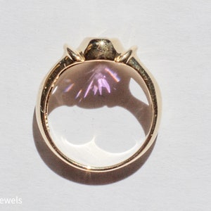 May include: A gold ring with a large, clear gemstone that has a purple hue. The ring is set in a bezel setting and has a simple band.