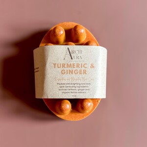 May include: A brown and orange bar soap with the text "ARCH AURA" and "TURMERIC & GINGER" on the label. The soap is packaged in a brown paper wrapper. The soap is 4 oz.
