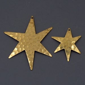 May include: Two gold-toned metal star-shaped charms with a hammered texture. The larger star is about twice the size of the smaller star.