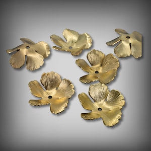 May include: Six brass-colored, leaf-shaped metal components with a central hole. The leaves have detailed veining and a matte finish. The components are arranged on a gradient gray background.