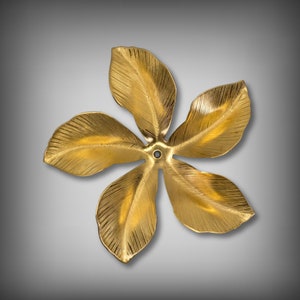 May include: A golden metal flower with five detailed petals. The petals are arranged in a star-like pattern, with a small hole in the center. The surface of the petals has a textured, veined appearance, giving it a realistic look.