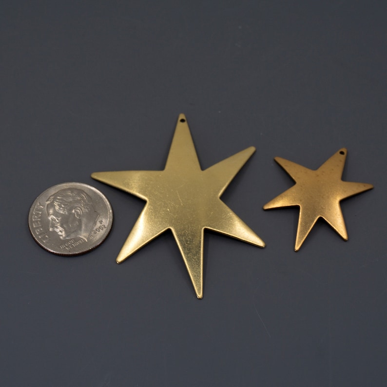 K&ouml;nnte beinhalten: Zwei goldfarbene Metallsterne mit einem Loch oben. Der gr&ouml;&szlig;ere Stern ist etwa so gro&szlig; wie eine deutsche Zehn-Cent-M&uuml;nze.