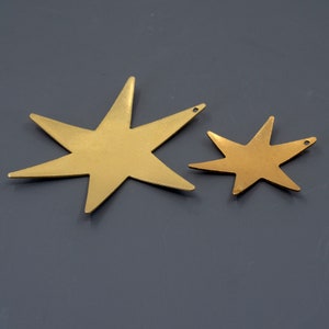 K&ouml;nnte beinhalten: Zwei goldene Sternformen aus Metall, eine gr&ouml;&szlig;er als die andere, auf grauem Hintergrund.