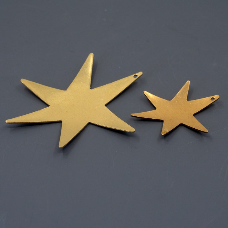 K&ouml;nnte beinhalten: Zwei goldene Sternformen aus Metall, eine gr&ouml;&szlig;er als die andere, auf grauem Hintergrund.