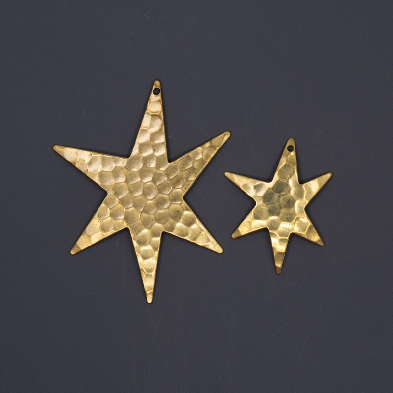 May include: Two gold metal star-shaped charms with a hammered texture. The larger star is about 2 inches wide and the smaller star is about 1 inch wide.
